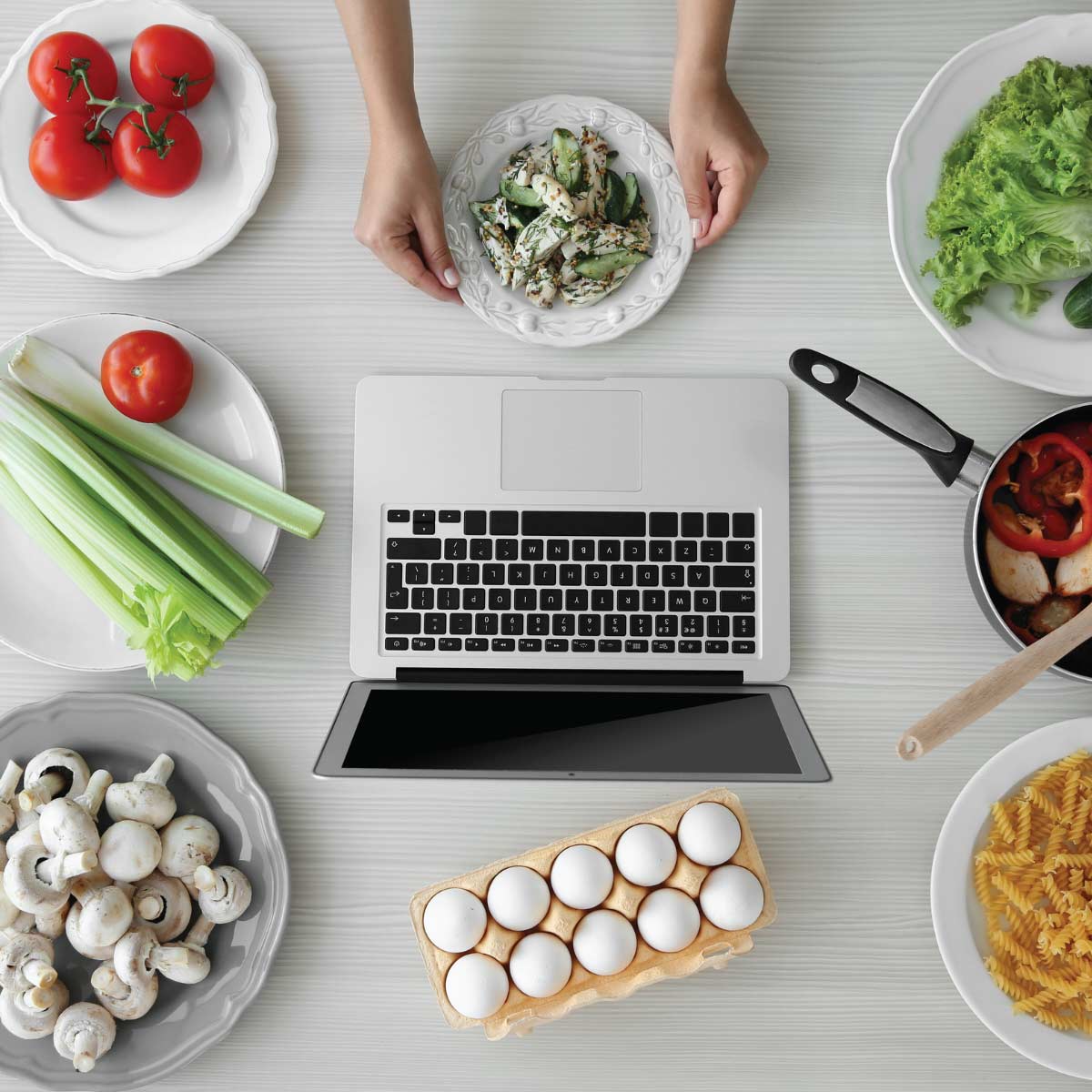 Laptop open on a counter with various bowls and dishes of food spread around it.