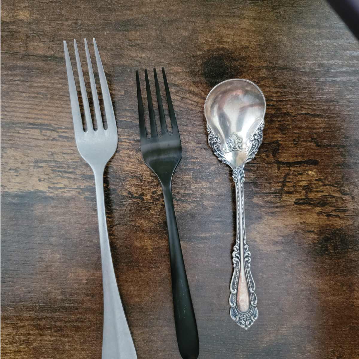 2 forks that are not shiny with no reflection and one antique spoon that does have a reflection of my phone in it.