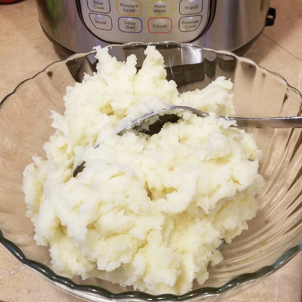 Plain mashed potatoes in a serving bowl very close up with the Instant Pot in the background.